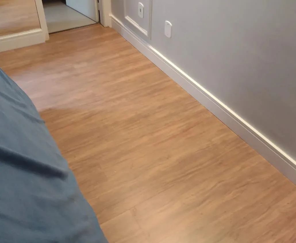 Corredor com piso de aspecto amadeirado e acabamento em rodapé branco.