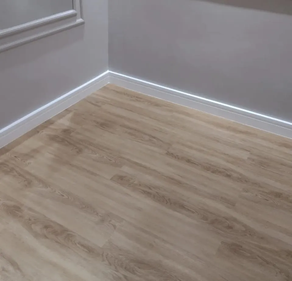 Piso de aspecto amadeirado, rodapé branco e boiserie na parede.