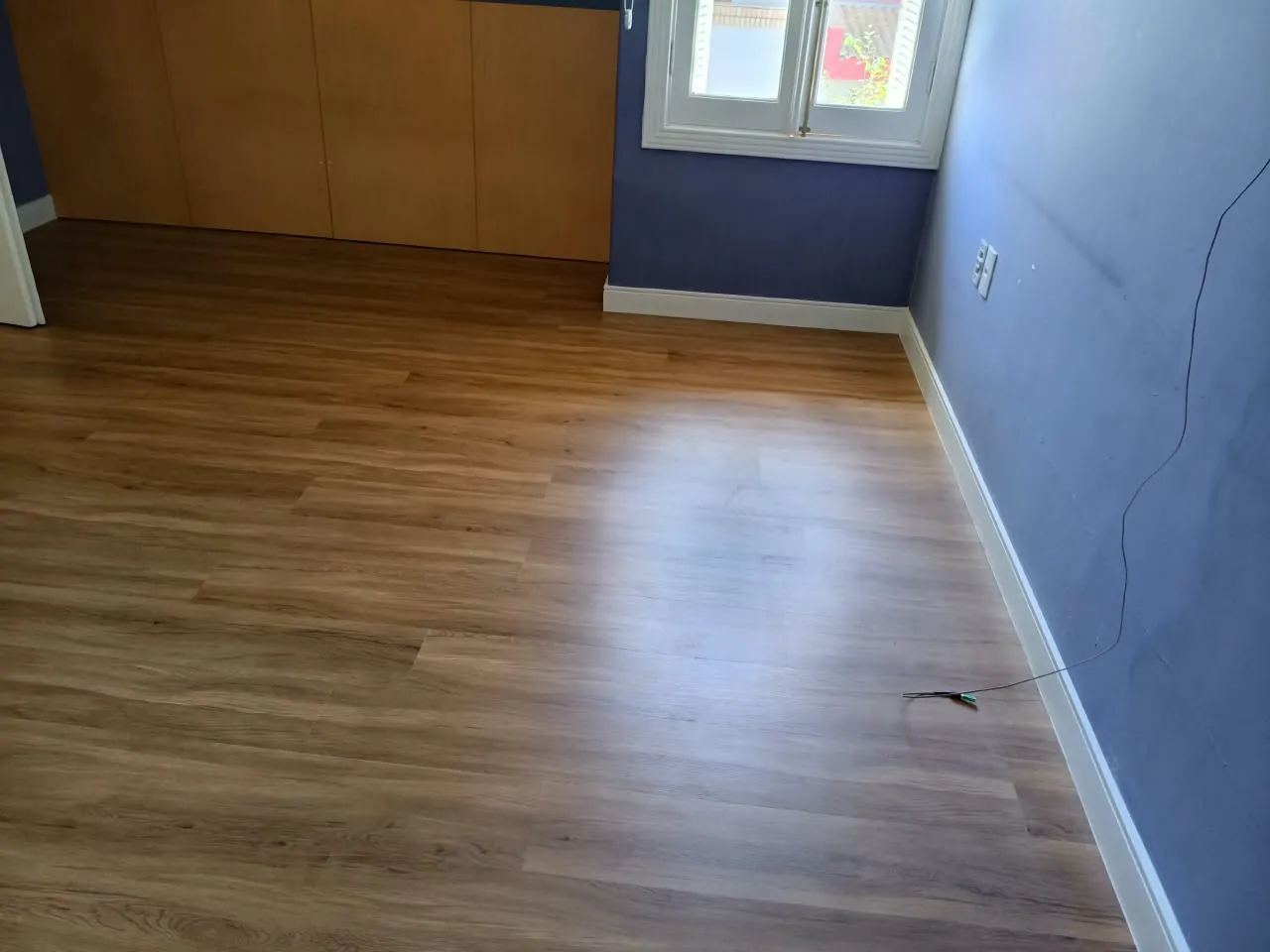 Quarto com piso de aspecto amadeirado, armário e parede azul.