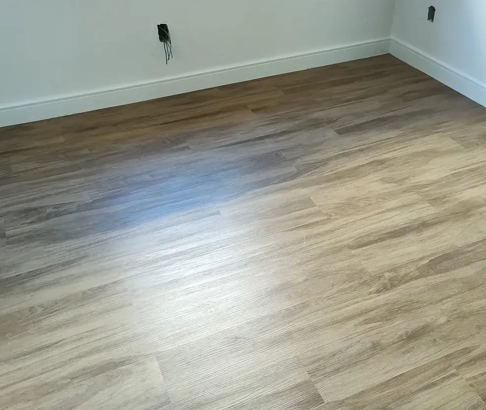 Quarto com piso de aspecto amadeirado claro e rodapé branco.