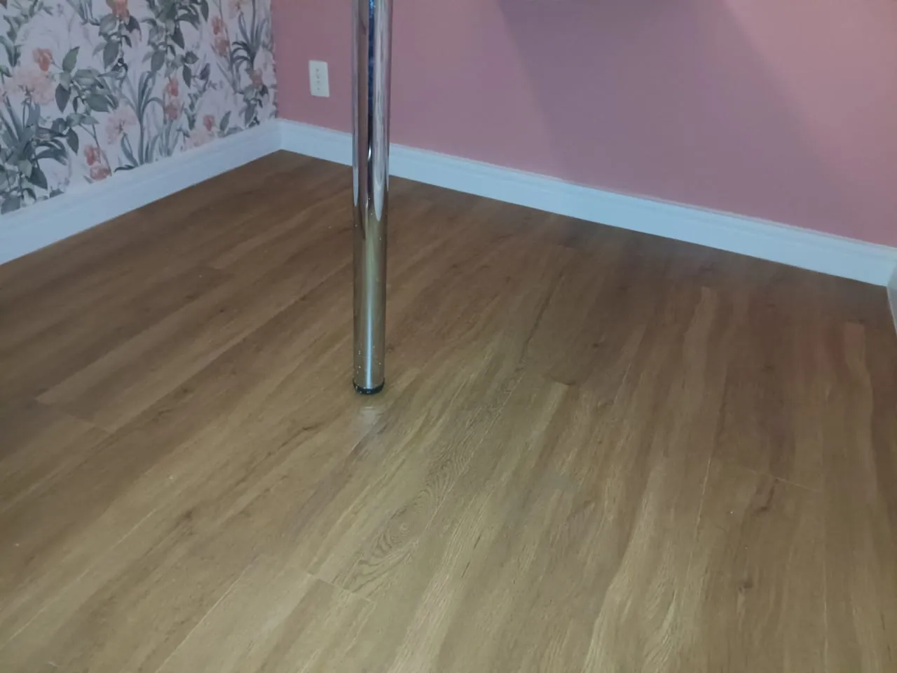 Piso de aspecto amadeirado em quarto com parede rosa e floral.