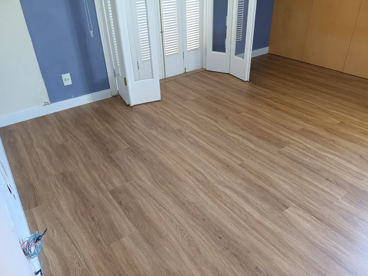Quarto com piso de aspecto amadeirado e portas brancas.